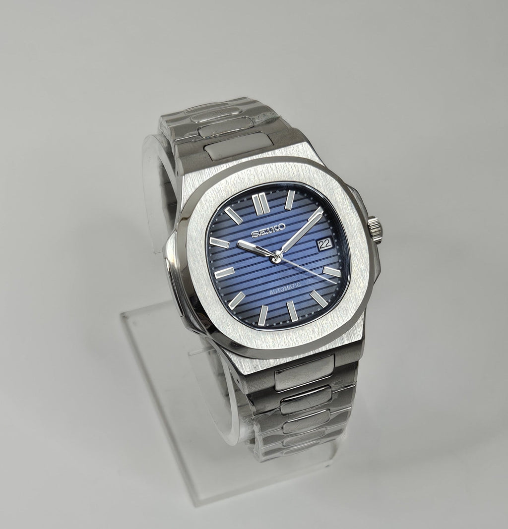 A custom Seiko Nautilus watch with a blue dial, stainless steel integrated bracelet, and a transparent case back displayed on a stand.