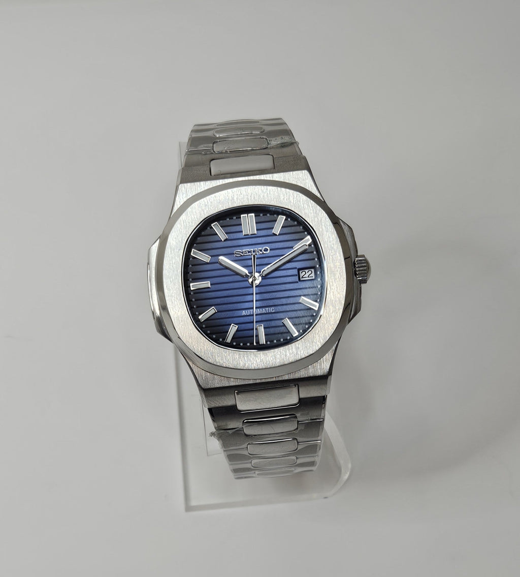A custom Seiko Nautilus watch with a blue dial, stainless steel integrated bracelet, and a transparent case back displayed on a stand.