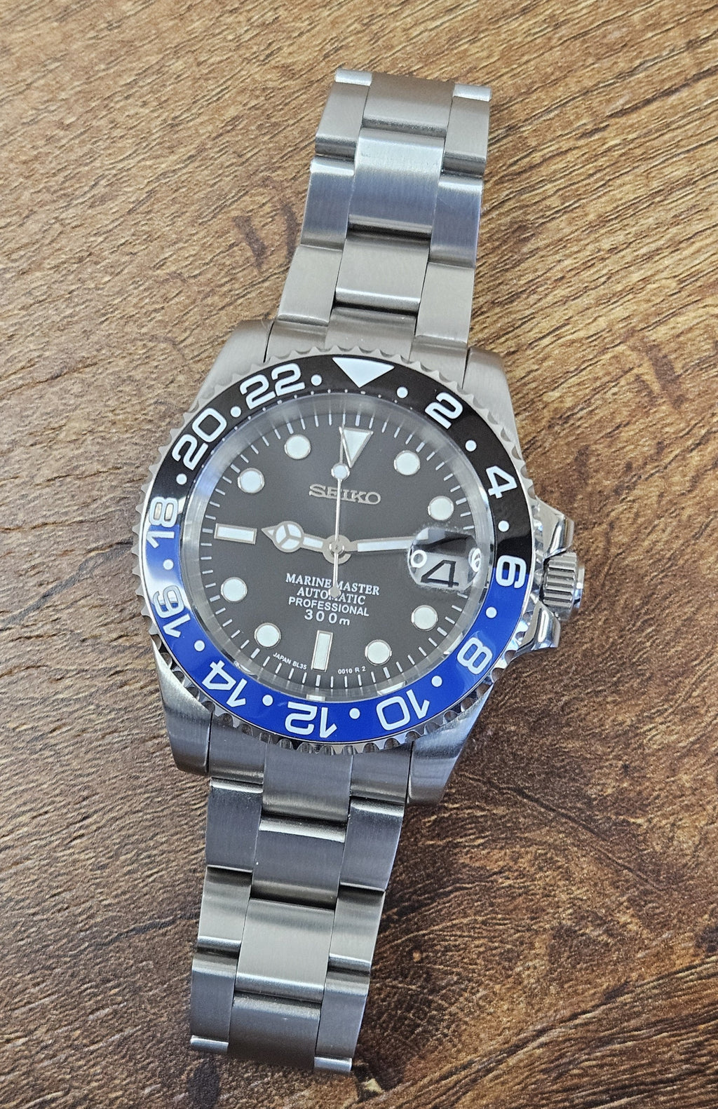 Silver Seiko watch with black and blue bezel on a wooden surface