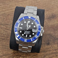 A steel watch with a blue ceramic bezel and a black sunburst dial, featuring silver hands and indexes, and a stainless steel bracelet.