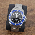 A steel watch with a blue ceramic bezel and a black sunburst dial, featuring silver hands and indexes, and a stainless steel bracelet.
