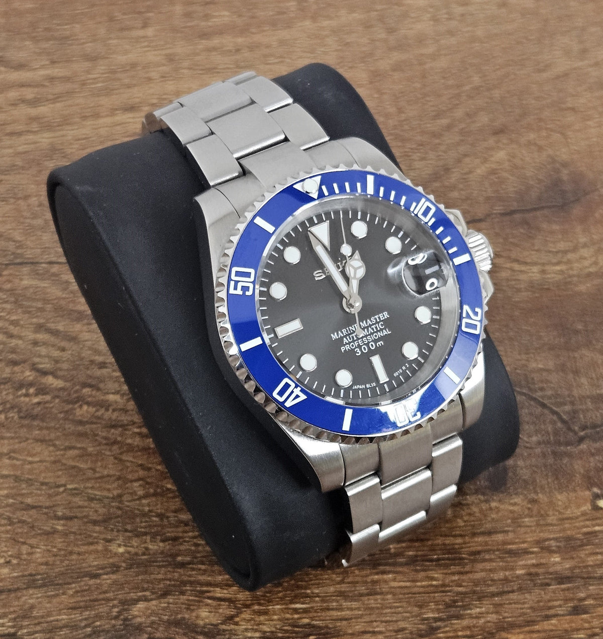 Wristwatch with blue bezel and silver band on wooden surface.