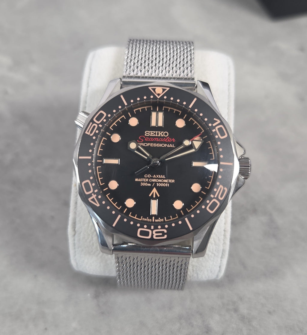 Seiko watch with black dial and silver mesh band on a gray background