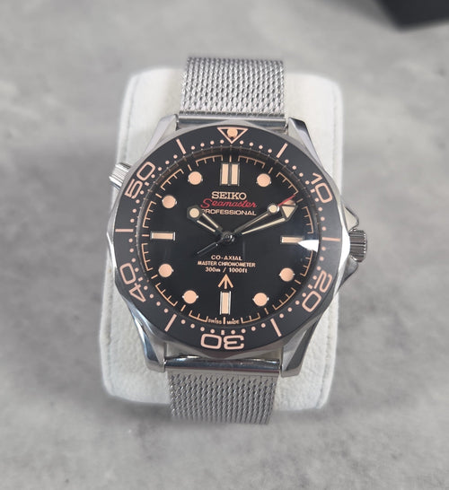 Seiko watch with black dial and silver mesh band on a gray background