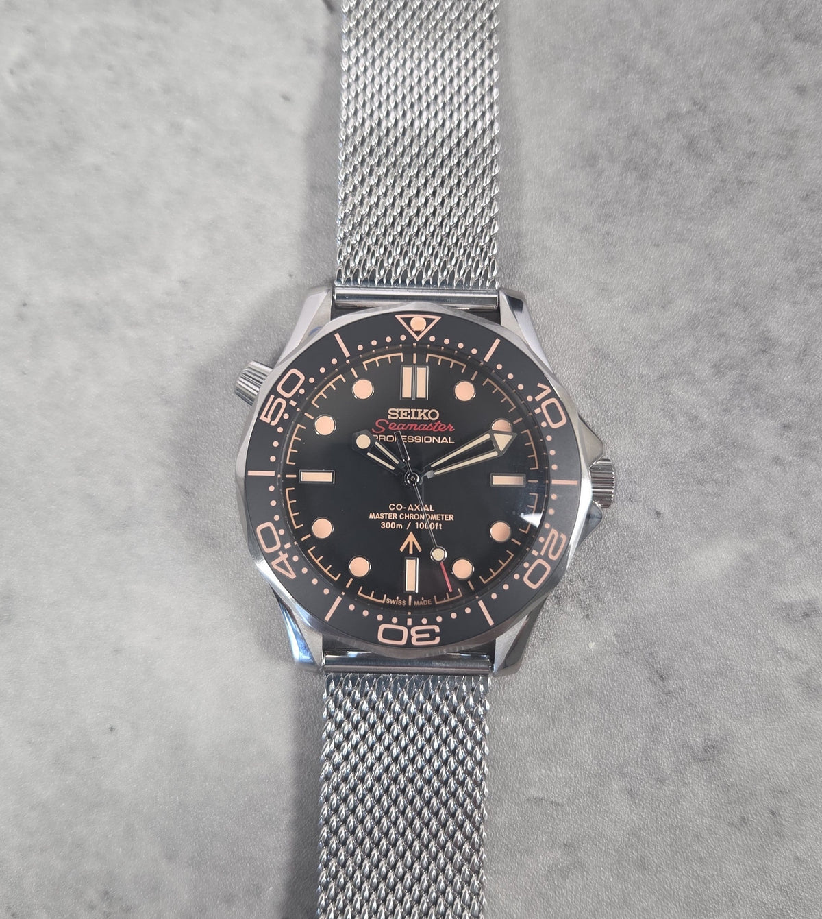 Seiko watch with black dial and silver mesh band on a gray background