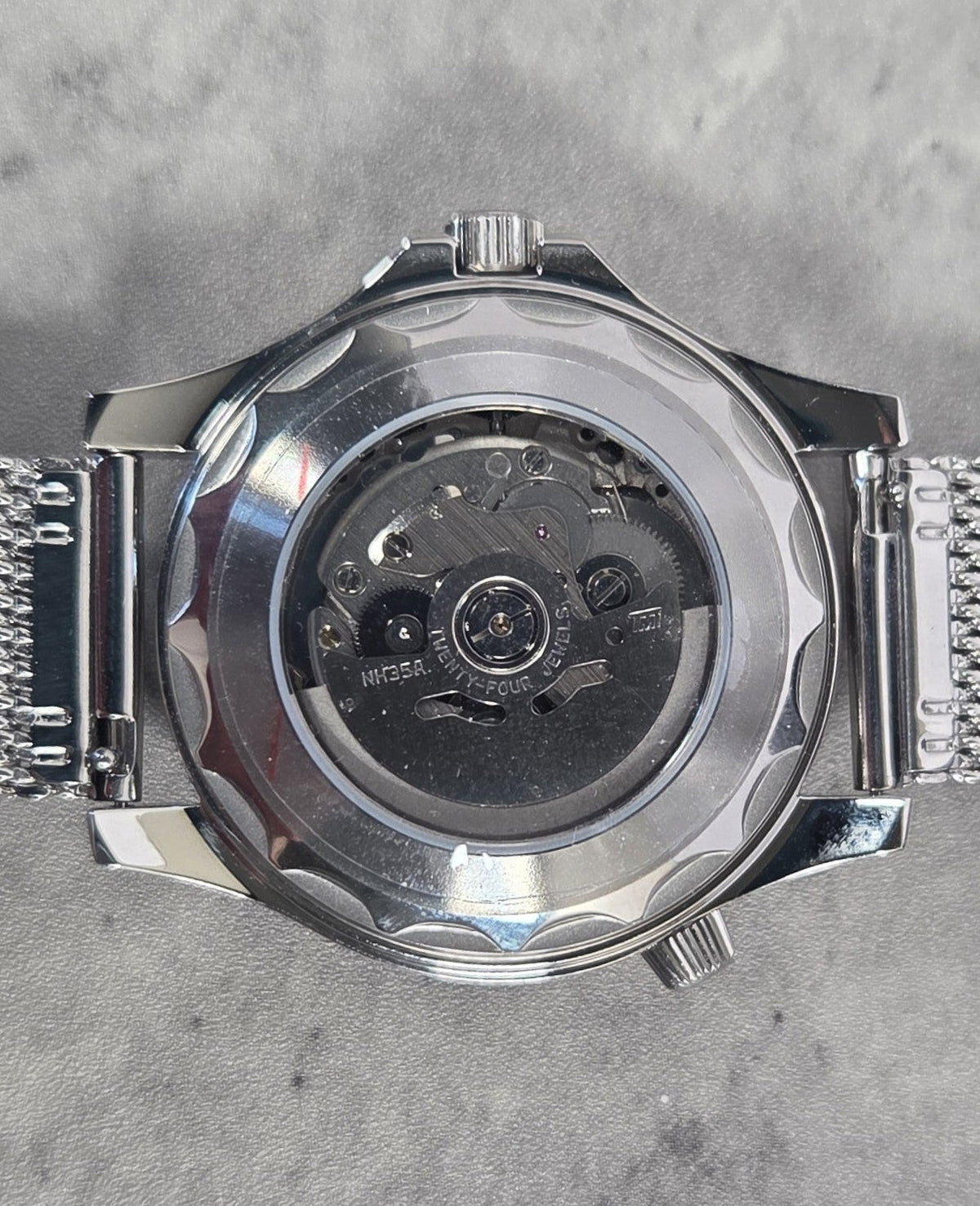 Silver watch with mesh band on a gray textured background