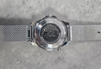 Silver watch with mesh band on a gray textured background