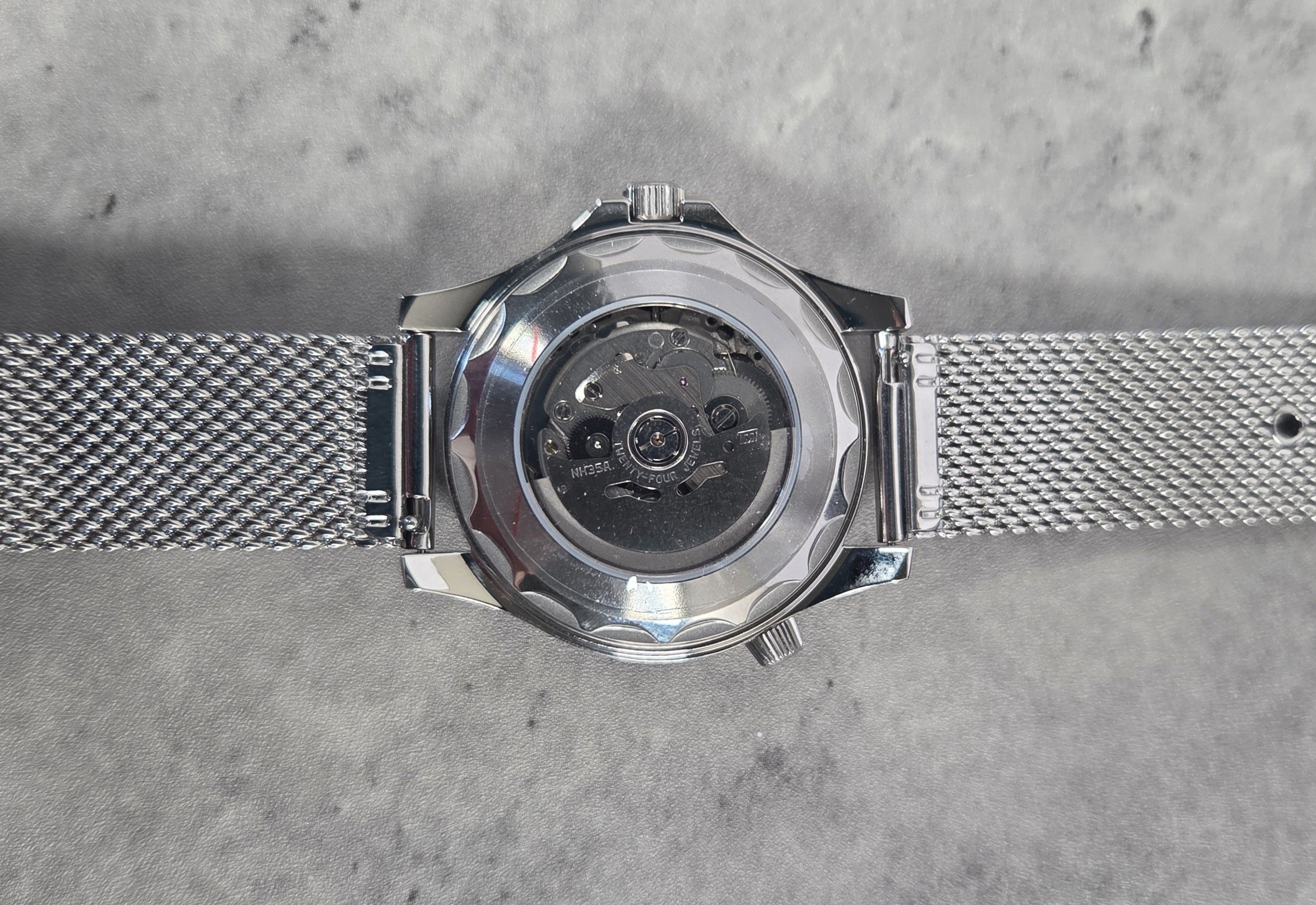 Silver watch with mesh band on a gray textured background
