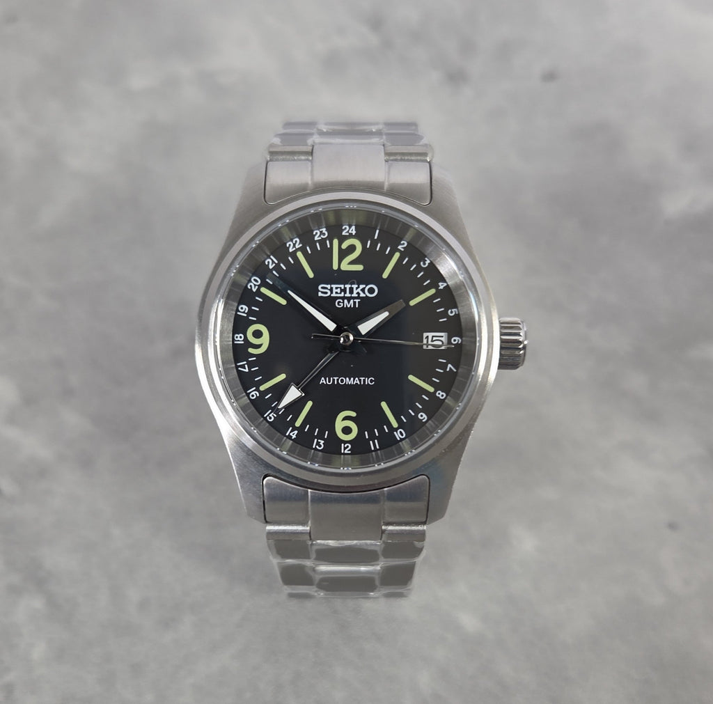 Seiko watch with black dial and silver metal strap on a gray background