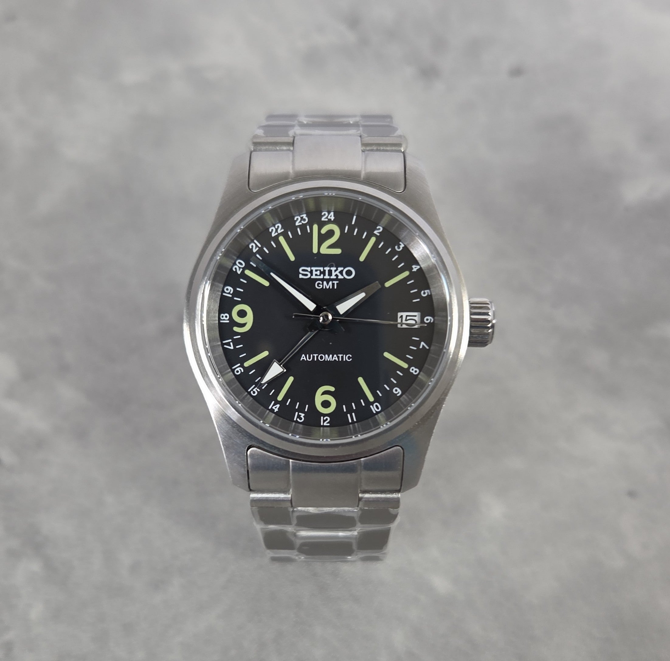 Seiko watch with black dial and silver metal strap on a gray background