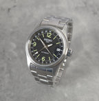 Seiko watch with black dial and silver metal strap on a gray background