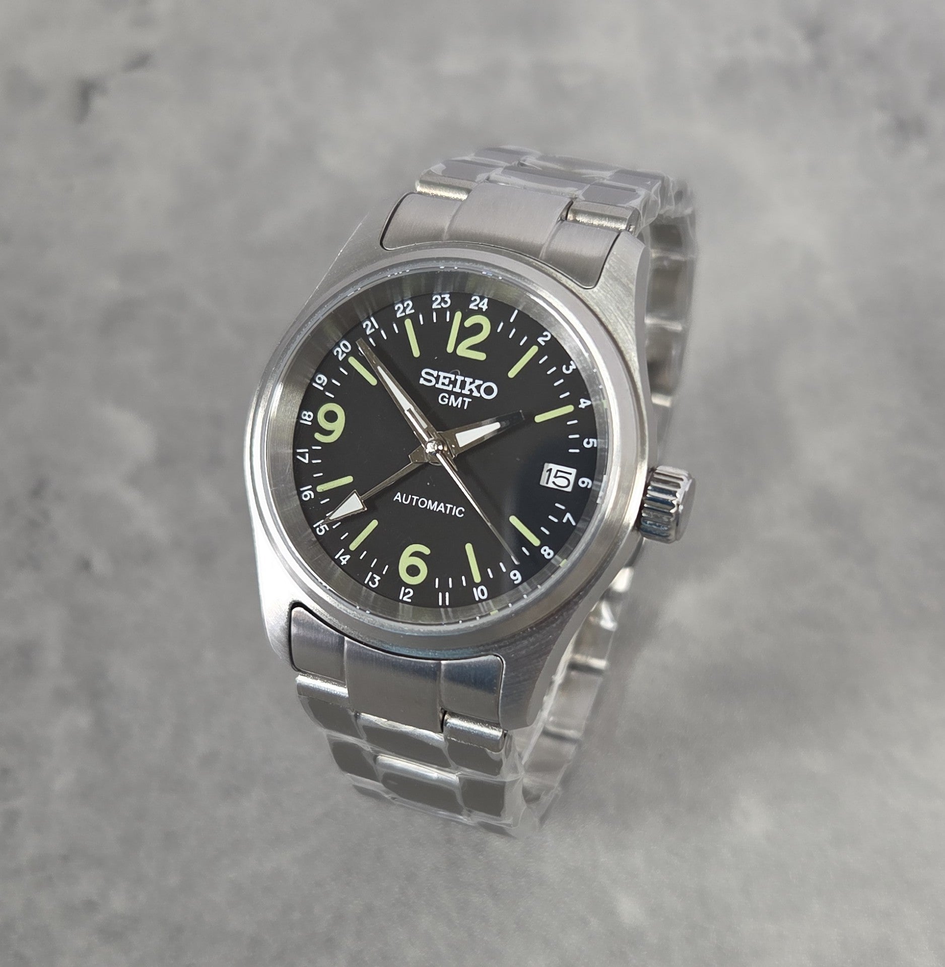Seiko watch with black dial and silver metal strap on a gray background