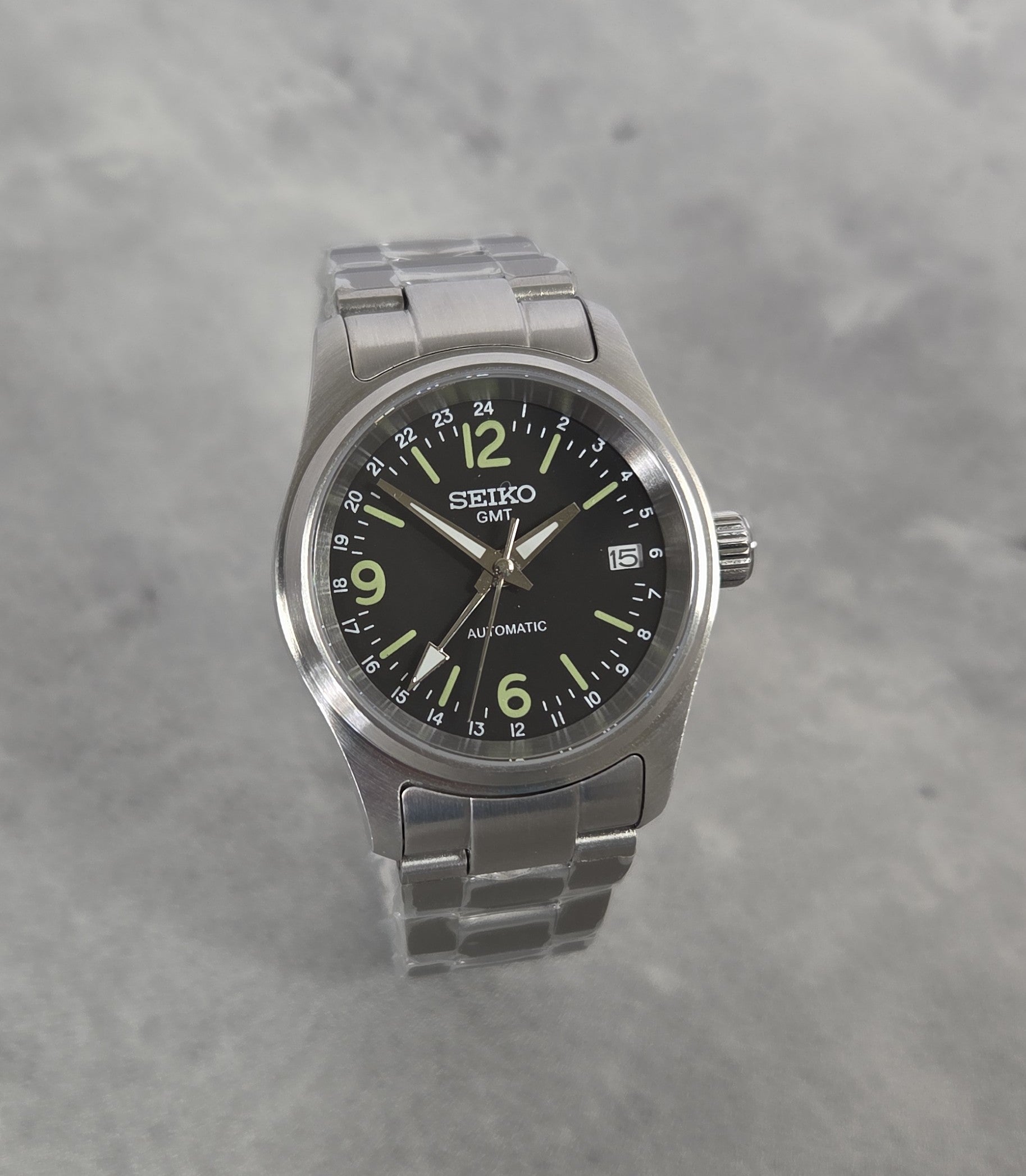 Seiko watch with black dial and silver metal strap on a gray background