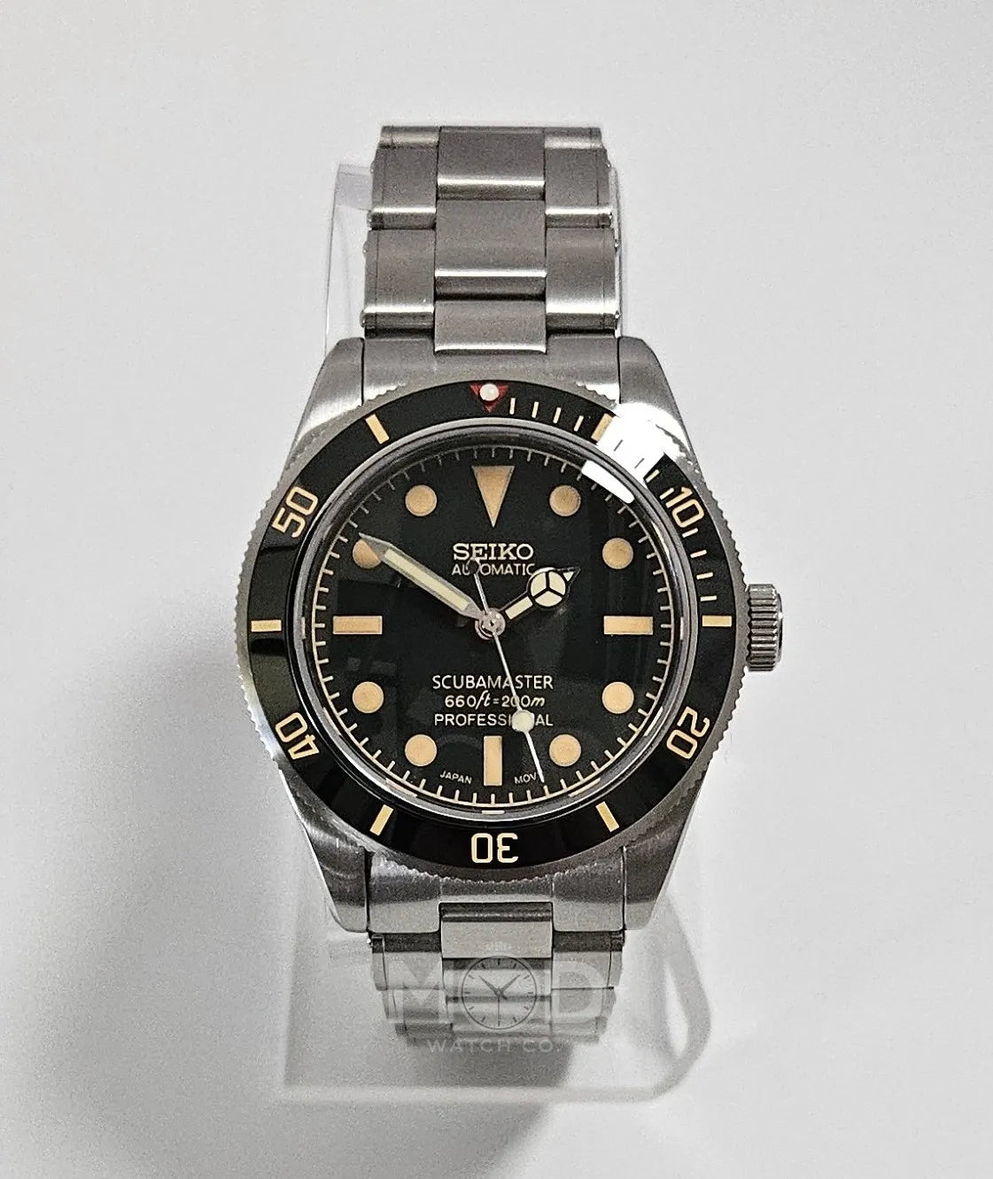 Seiko watch with black dial and silver metal strap on a light gray background