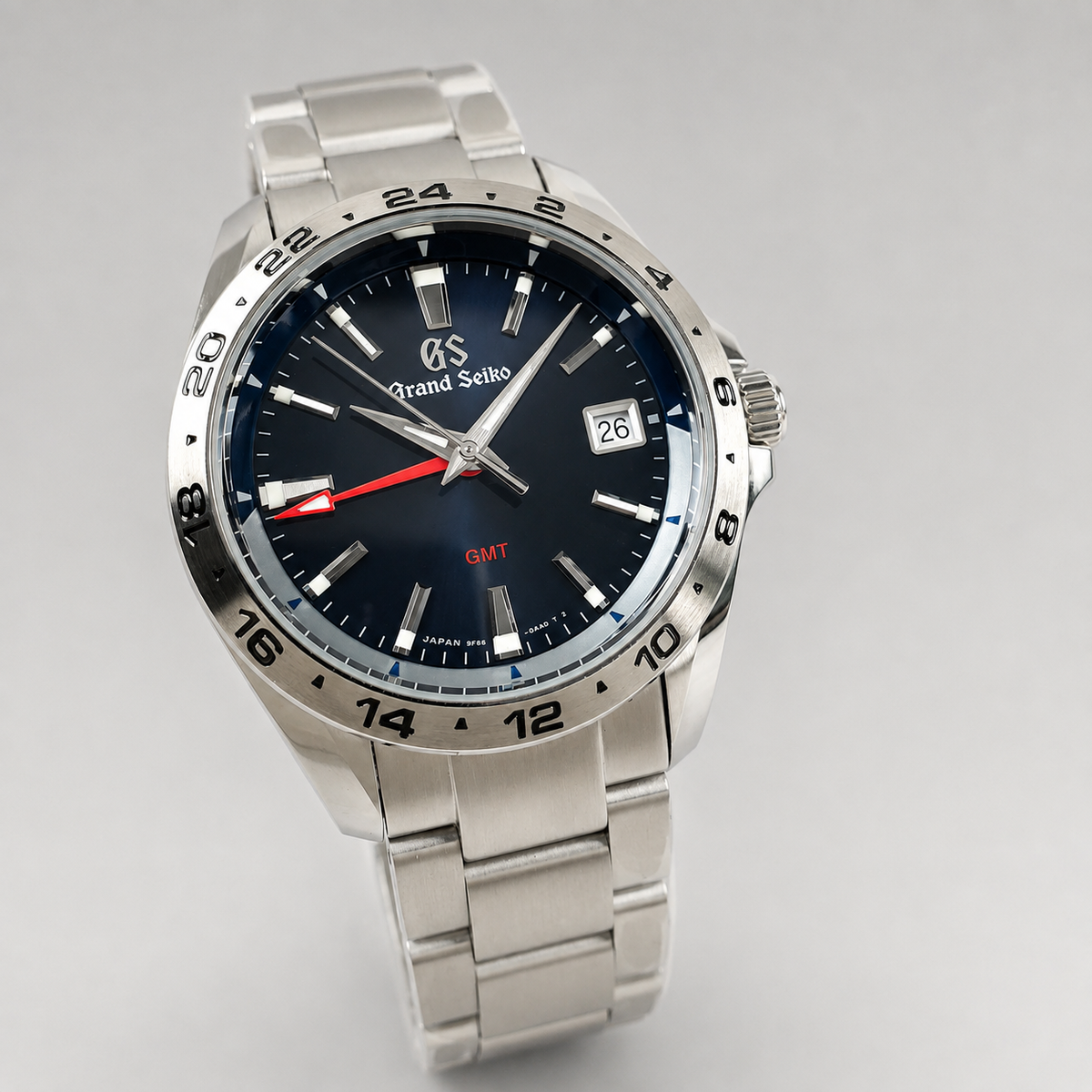 A Grand Seiko stainless steel wristwatch with a dark blue dial, silver-tone metal bracelet, and a black rotating bezel with white and red markings.