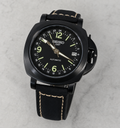 A Seiko GMT automatic watch with a black case, black dial, and black leather strap with light tan contrast stitching, photographed on a light gray marble surface.