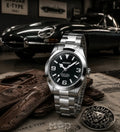 Silver Seiko watch with black dial on a surface with Jaguar E-Type car in the background