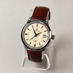Watch with brown leather strap on a clear stand against a light gray background