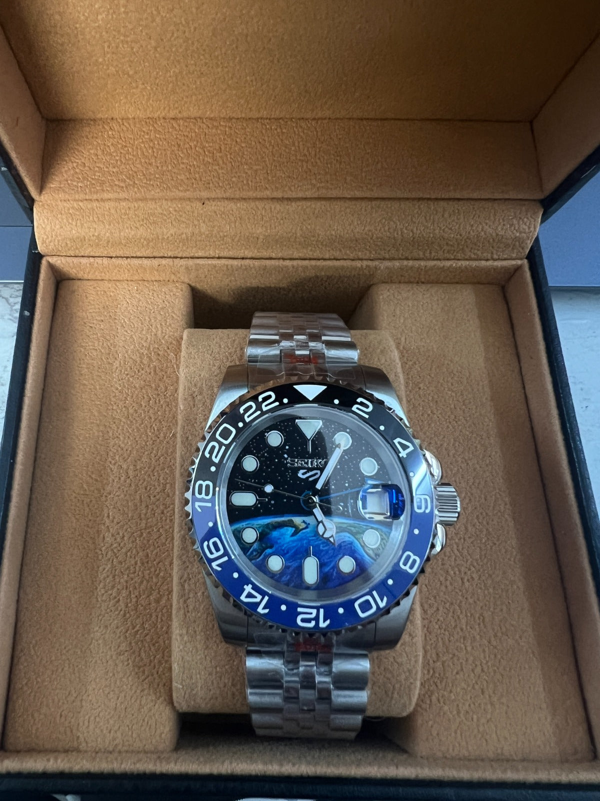 Luxury watch with blue bezel and silver case in a brown box