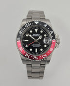 A GMT Master custom mod watch with a black dial, black and red bezel, and silver bracelet, displayed alongside a brown leather case, a cleaning brush, and a watch pen.