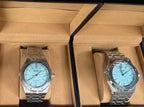 Two silver watches with blue faces in a brown box