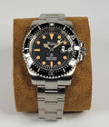 Silver Seiko watch with black dial on a brown cushion against a white background