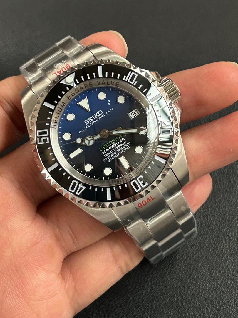 Silver Seiko watch with black dial held in a hand against a dark background
